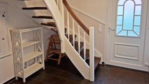 A staircase with white railings and wooden steps, a white door with a window, and a white shelving unit. - Deichhuus in Nessmersiel (Dornum)