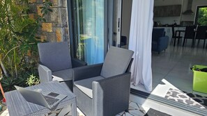 Eine Terrasse mit Korbmöbeln, einem Laptop und einer grünen Mülltonne.