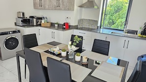 A modern kitchen with a built-in washer, a dining area with a table and chairs, and a window with a view of greenery. - Marvelous 3-bedroom apartment with AC in Grand Baie (Grand Baie)
