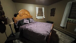 Een slaapkamer met een bed, nachtkastje, lamp, raam met gordijnen, en een wandradiator.