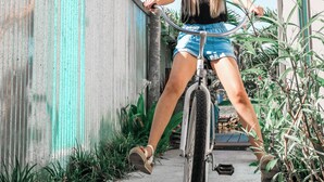 A person riding a bicycle on a sidewalk next to a building with a corrugated metal wall and a palm tree.