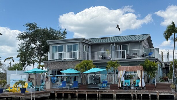 A waterfront property with a two-story building, a dock, and outdoor seating.
