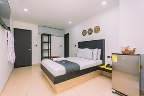 Una habitación de hotel moderna con una cama, un escritorio pequeño, un refrigerador y una puerta.