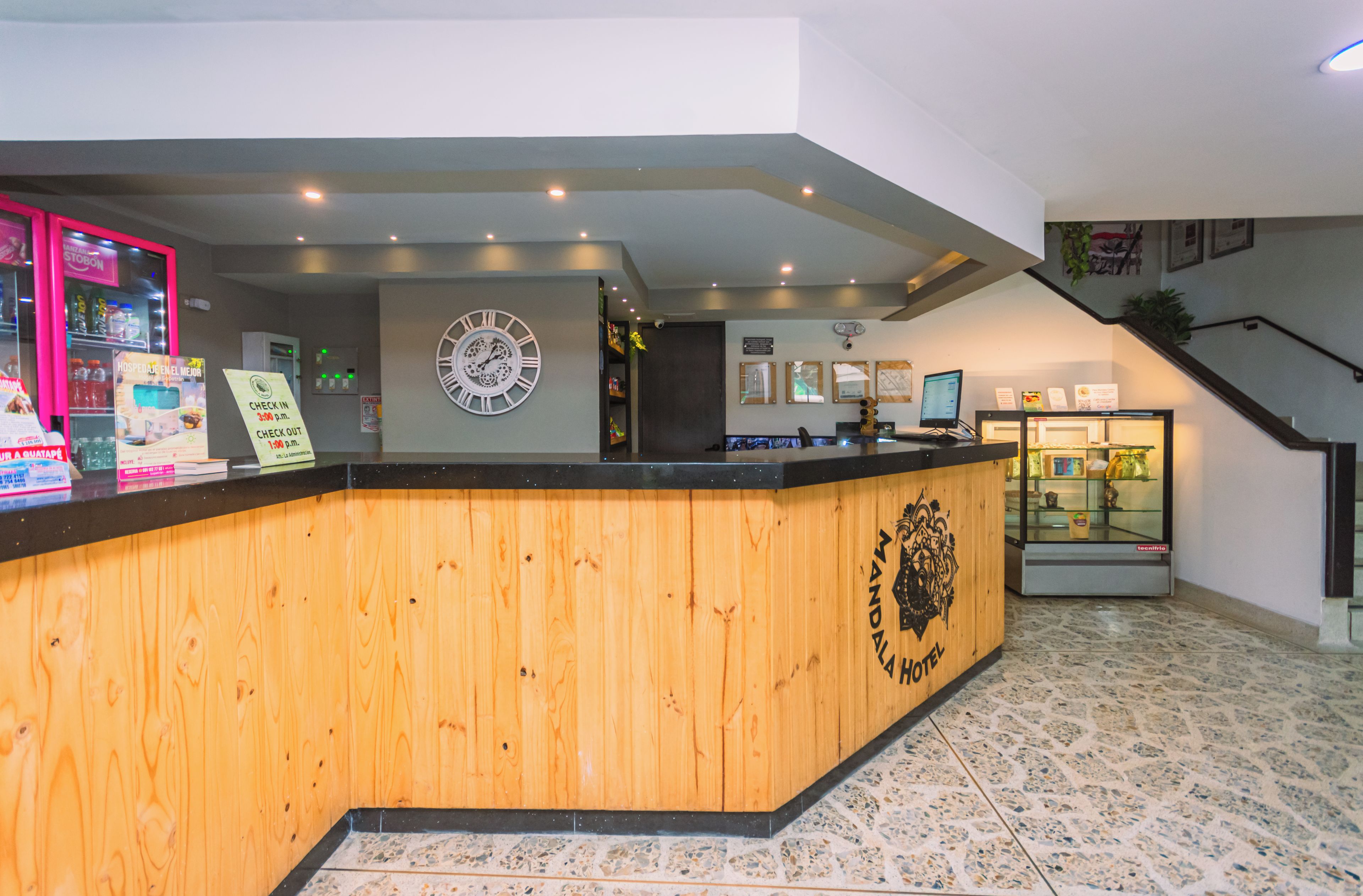 A hotel reception desk with a wooden counter, a clock, and a reception area with a staircase.