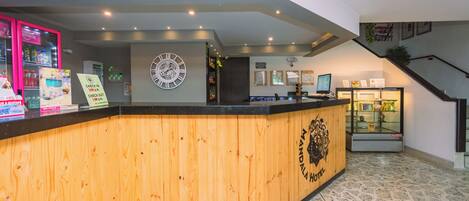 A hotel reception desk with a wooden counter, a clock, and a reception area with a staircase.