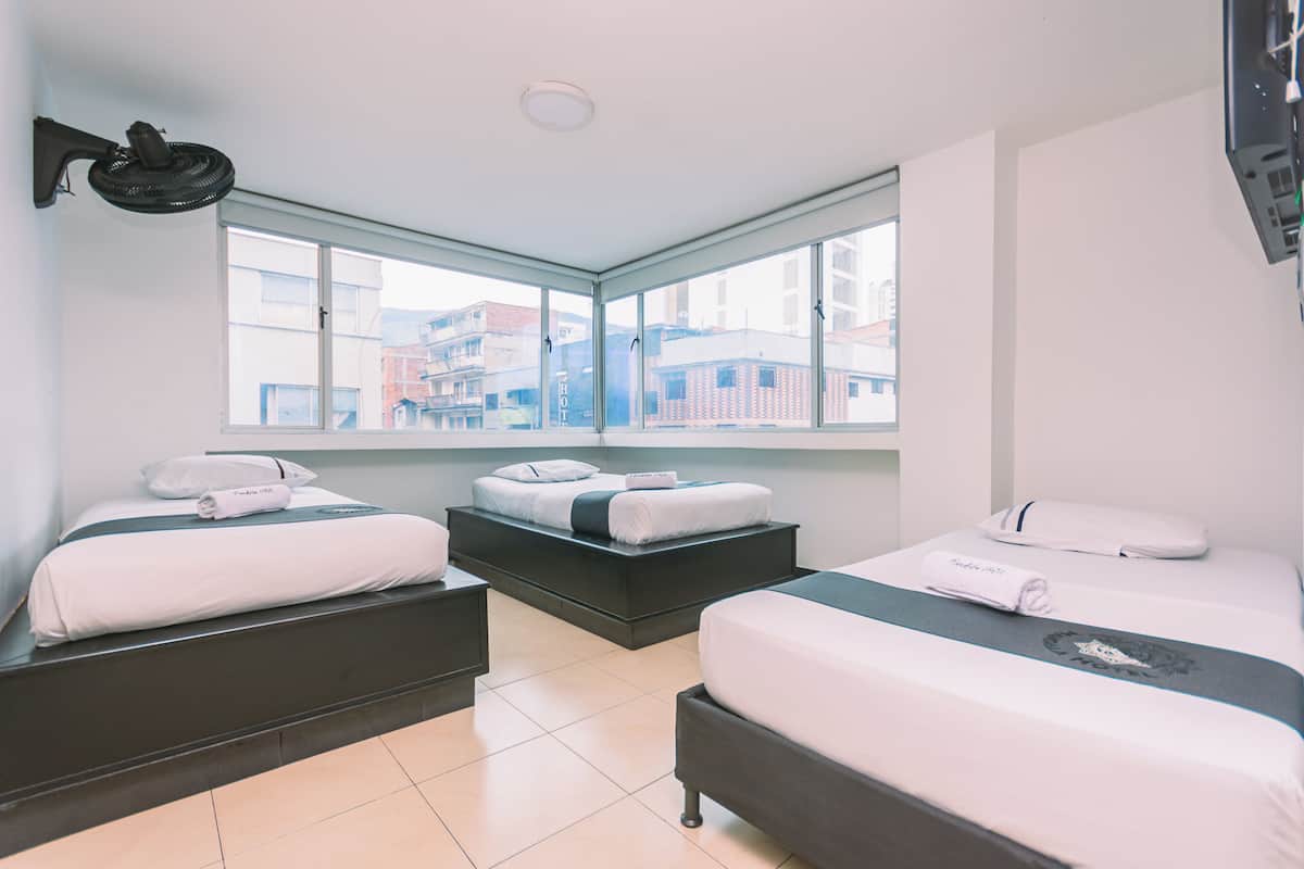 Habitación de hotel con dos camas, un ventanal grande y vistas a edificios.