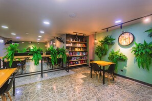 Un interior moderno con una estantería central, mesas, sillas y plantas verdes.
