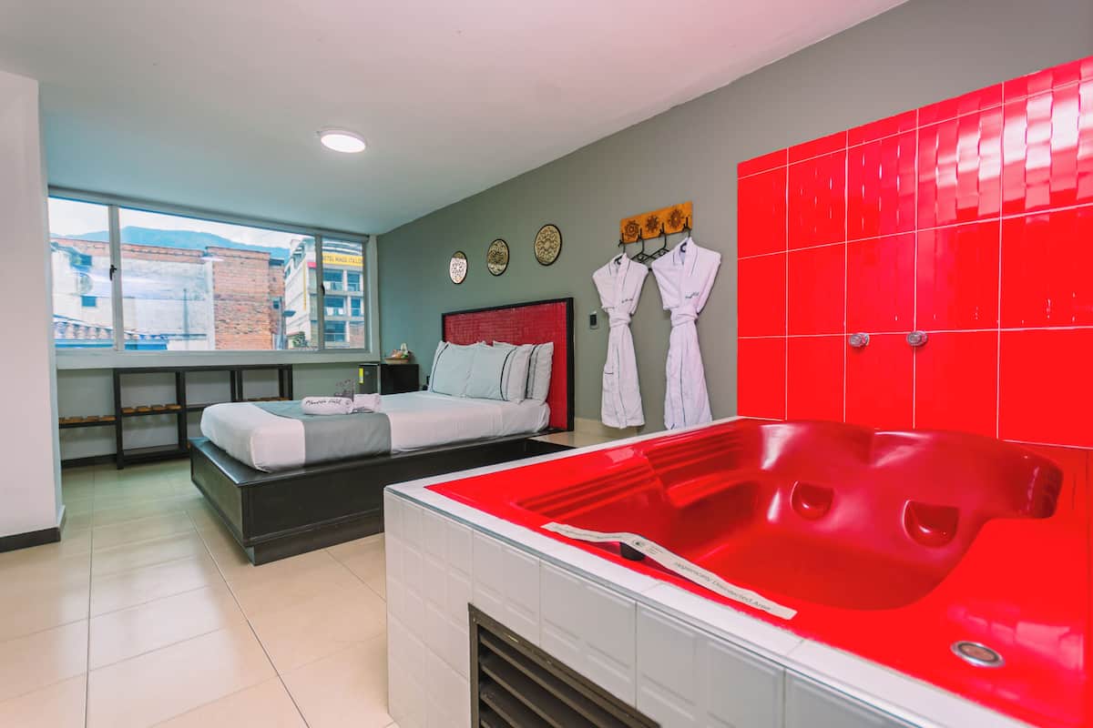 Habitación de hotel con cama, una bañera roja y ventana con vistas a edificios.