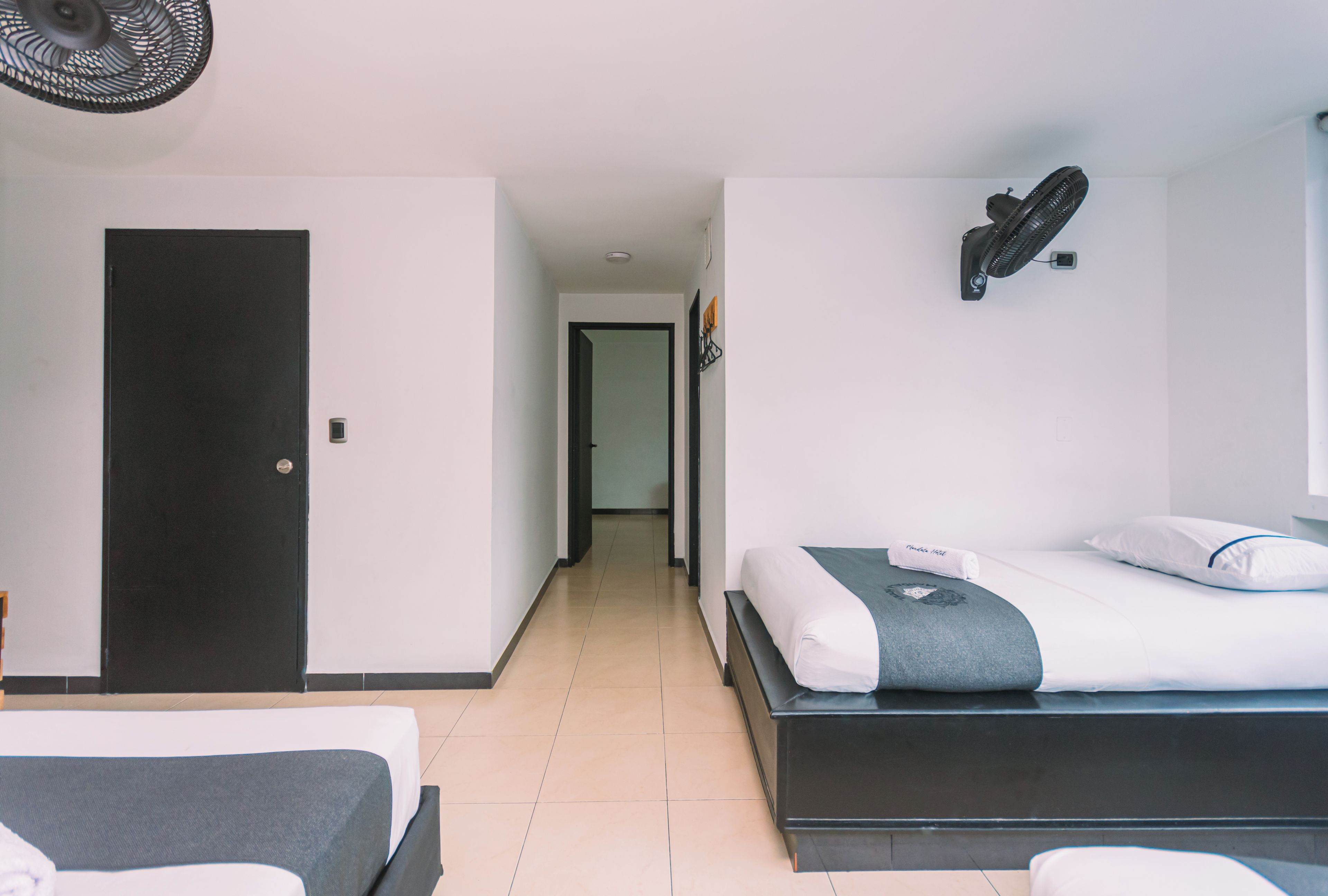 Une chambre d’hôtel avec un lit, une table de chevet, une porte et un ventilateur fixé au mur.