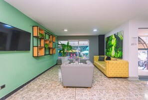 A lobby with a grey sofa, a yellow sofa, a TV, a plant, and a window with a view of the outside. - Mandala Medellín Centro By Gyc Hotels (Medellín)