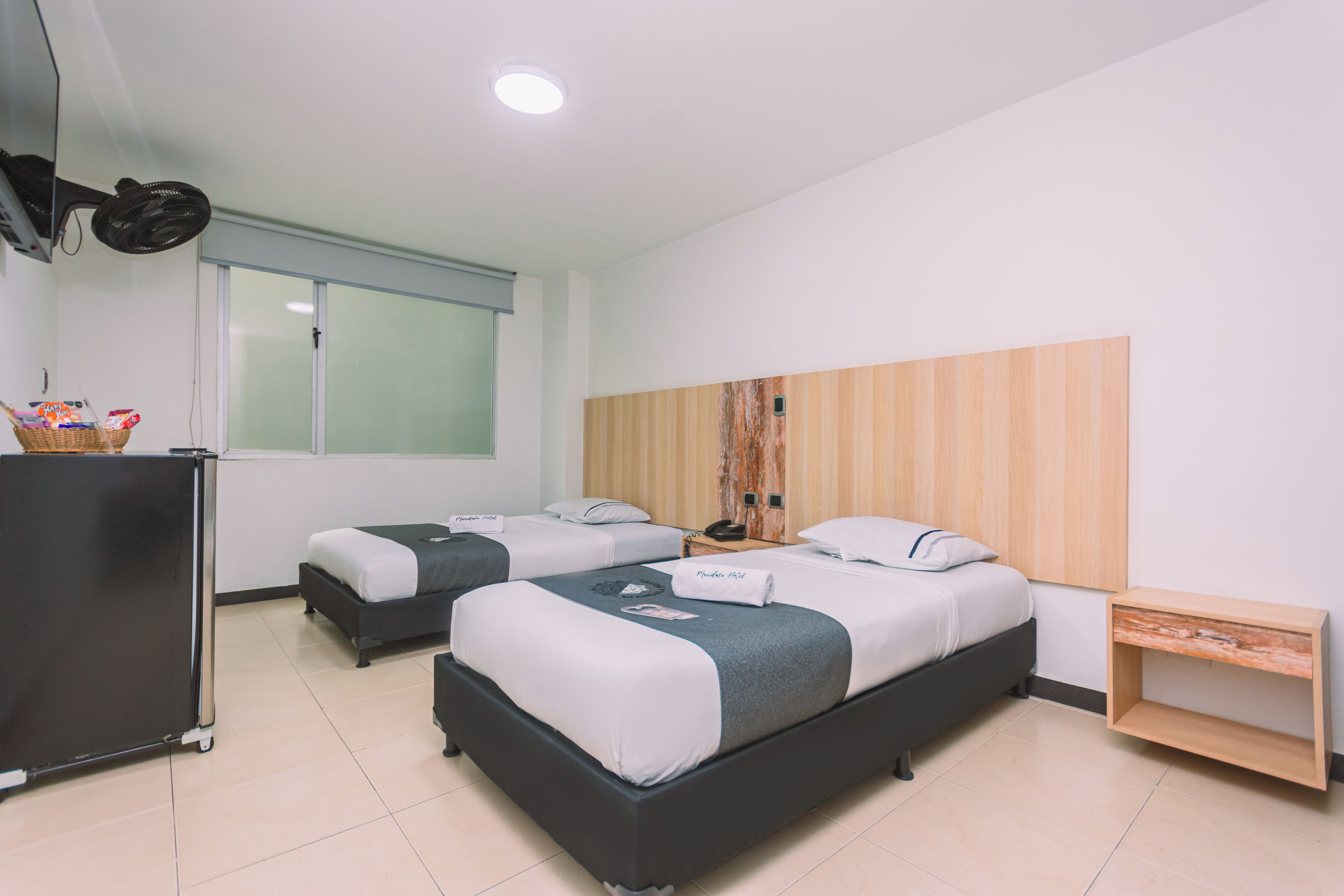 Habitación de hotel con dos camas, un escritorio pequeño, un refrigerador y una ventana con persianas.