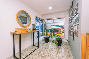A hallway with a wooden table, a mirror, potted plants, and a window with a view of a colorful train. - Mandala Medellín Centro By Gyc Hotels (Medellín)