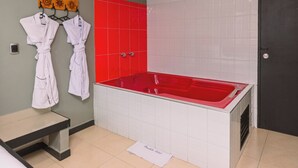 A modern bathroom with a red bathtub, white tiles, and a towel rack with robes. - Mandala Medellín Centro By Gyc Hotels (Medellín)