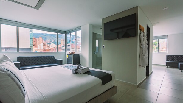 A modern hotel room with a large bed, a seating area, a TV, and a city view. - Mandala Medellín Centro By Gyc Hotels (Medellín)