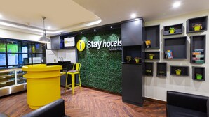 A reception area with a 'Stay hotels' sign, a yellow counter, a reception desk, a chair, and a wall with shelves holding potted plants. - Istay Hotels Jubilee Hills Hyderabad by Othpl (Hyderabad)