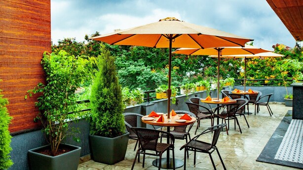 An outdoor patio with round tables and chairs, covered by large umbrellas, surrounded by potted plants and greenery. - Istay Hotels Jubilee Hills Hyderabad by Othpl (Hyderabad)
