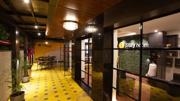 A hotel lobby with a yellow patterned floor, a reception desk, and a staircase leading to the upper floor.