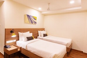 Ein Hotelzimmer mit zwei Betten, einem Holzkopfteil, einem Nachttisch mit Lampe, einem Telefon und einem Deckenventilator.