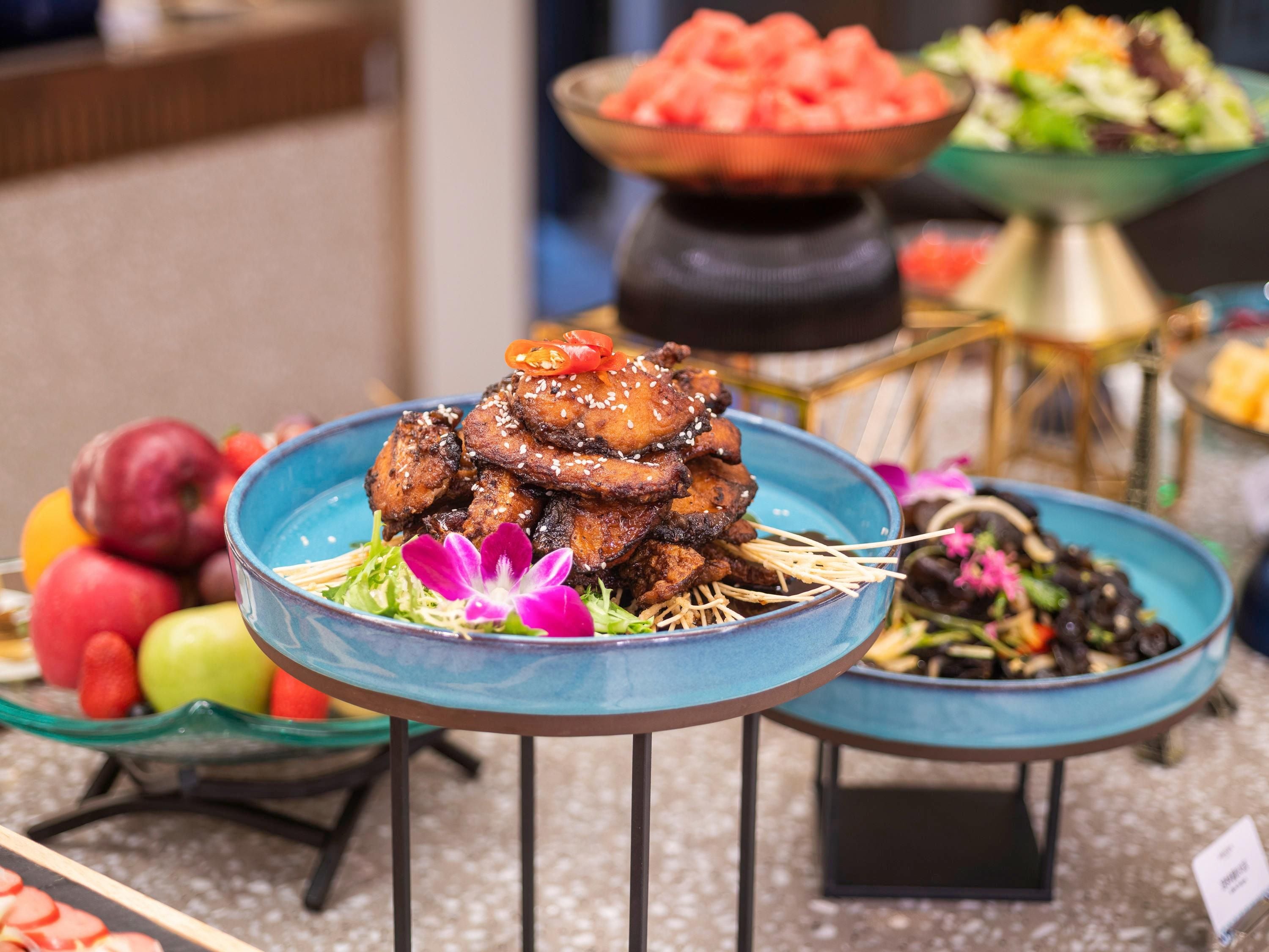 A buffet with various dishes, including a prominent plate of glazed meat with sesame seeds.
