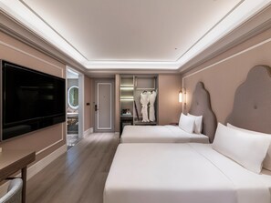 Une chambre d’hôtel dotée d’une grande télévision à écran plat, de deux lits, d’un dressing et d’une salle de bain avec un miroir.