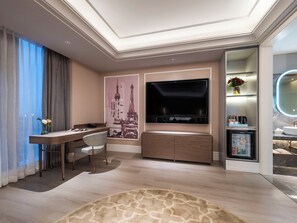 Habitación de hotel moderna con televisor de pantalla plana, escritorio con silla, minibar y un amplio ventanal con cortinas.