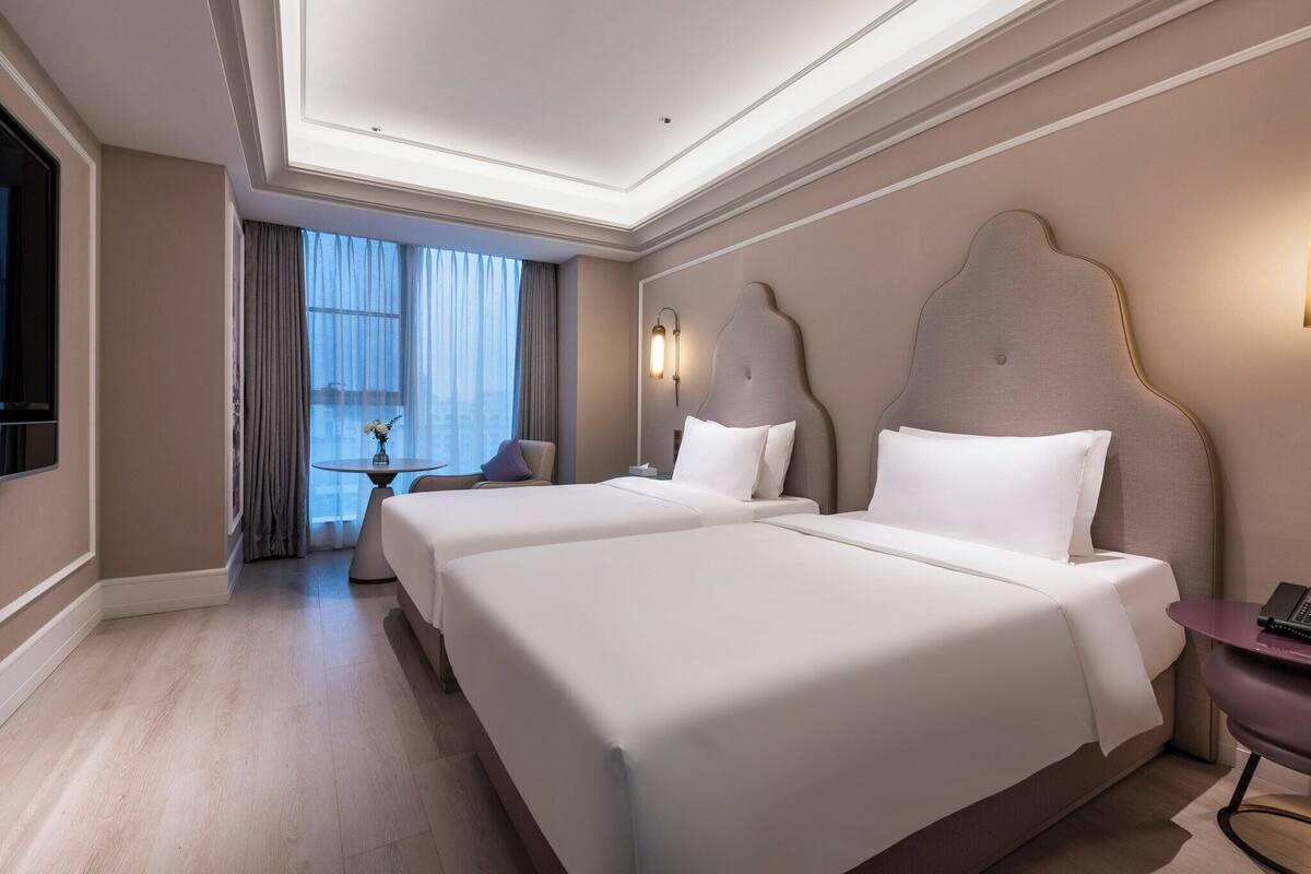 Habitación de hotel con dos camas, una mesita, una silla, televisión y ventana con cortinas.