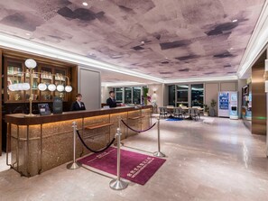 Un hall d’accueil d’hôtel avec un sol en marbre, un comptoir d’accueil, un espace salon et un distributeur automatique.