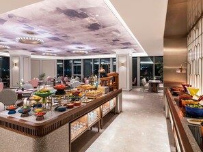 A modern hotel lobby with a long buffet table, seating area, and a ceiling with a unique design. - Mercure Shanghai Waigaoqiao (Shanghai)