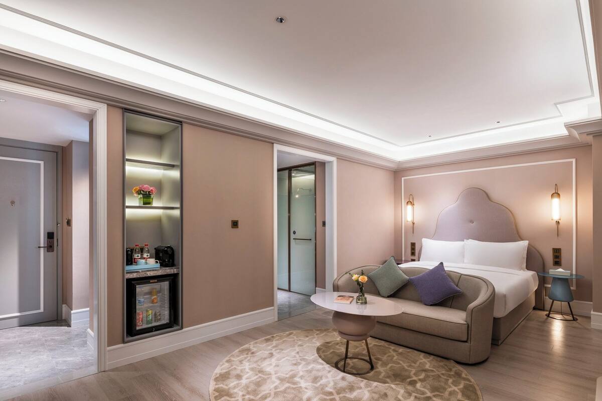 Una habitación de hotel moderna con cama, una pequeña mesa redonda, un sofá, una cafetera y un minibar.
