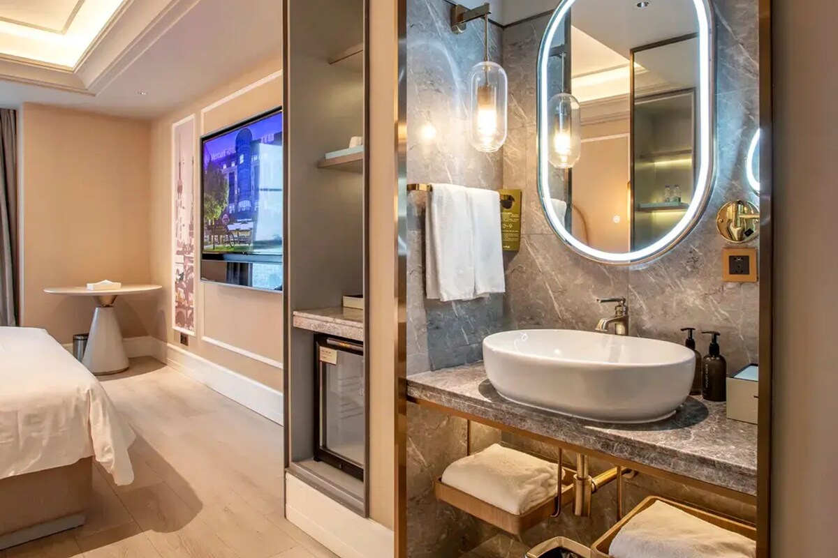 Une salle de bain d’hôtel moderne, dotée d’un grand miroir ovale, d’un lavabo blanc et d’un comptoir en marbre.