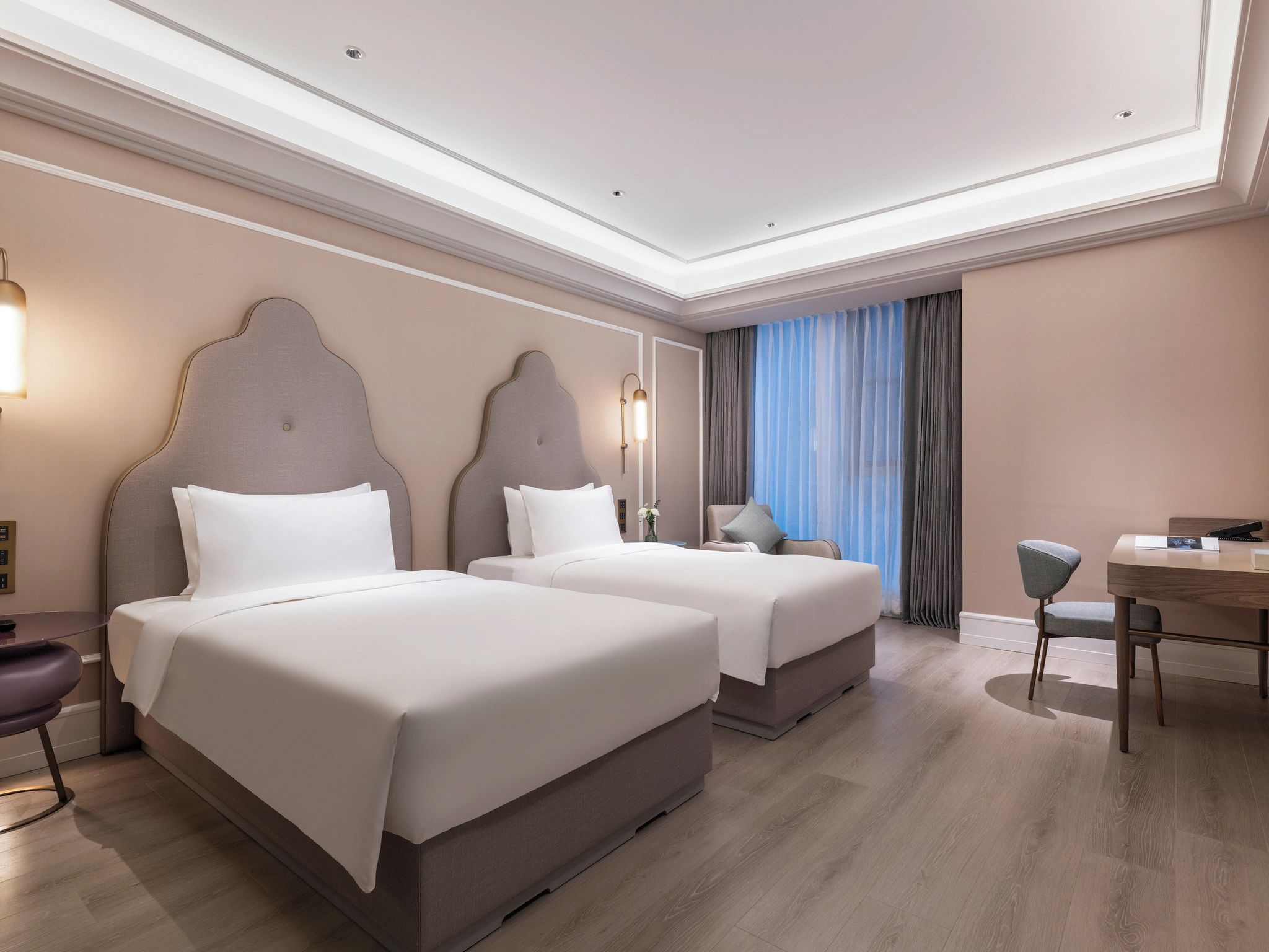 Habitación de hotel con dos camas, un escritorio, una silla y un ventanal con cortinas.