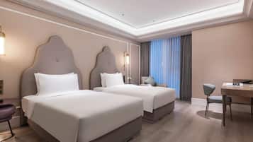 A hotel room with two beds, a desk, a chair, and a large window with curtains.