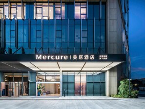 L’entrée d’un hôtel, avec une façade moderne, de grandes fenêtres en verre et une enseigne bien visible.