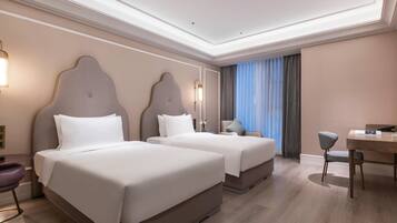 A hotel room with two beds, a desk, a chair, and a large window with curtains.
