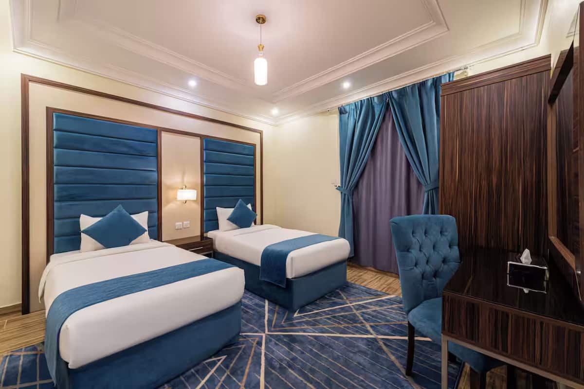 A hotel room with two beds, a desk, a chair, and a large mirror.