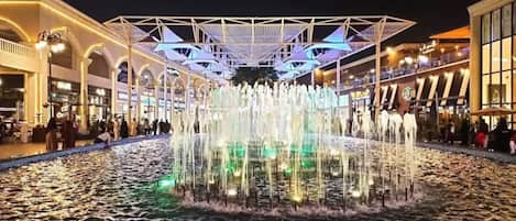 Una fuente de agua con una estructura geométrica en su parte superior, rodeada por una piscina reflectante.