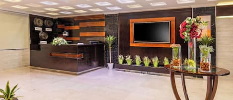 A reception area with a modern desk, a flat-screen TV, and decorative plants.
