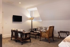 A room with a television mounted on the wall, a sofa, a chair, a small table, and a lamp. - The Cape Town Club (Cape Town)