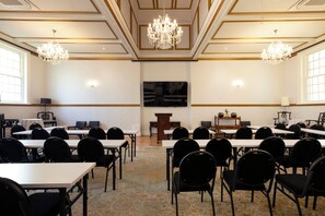 Un salón de conferencias con mesas, sillas, un atril y candelabros.
