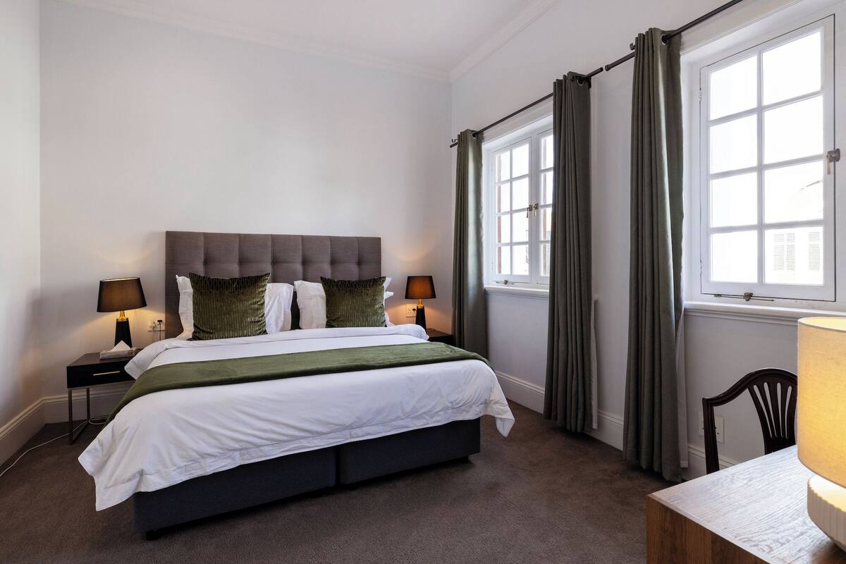 A neatly arranged bedroom with a bed, two bedside tables with lamps, a chair, and a window with curtains.