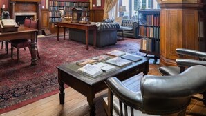 A library with a fireplace, leather chairs, a wooden desk, and bookshelves. - The Cape Town Club (Cape Town)