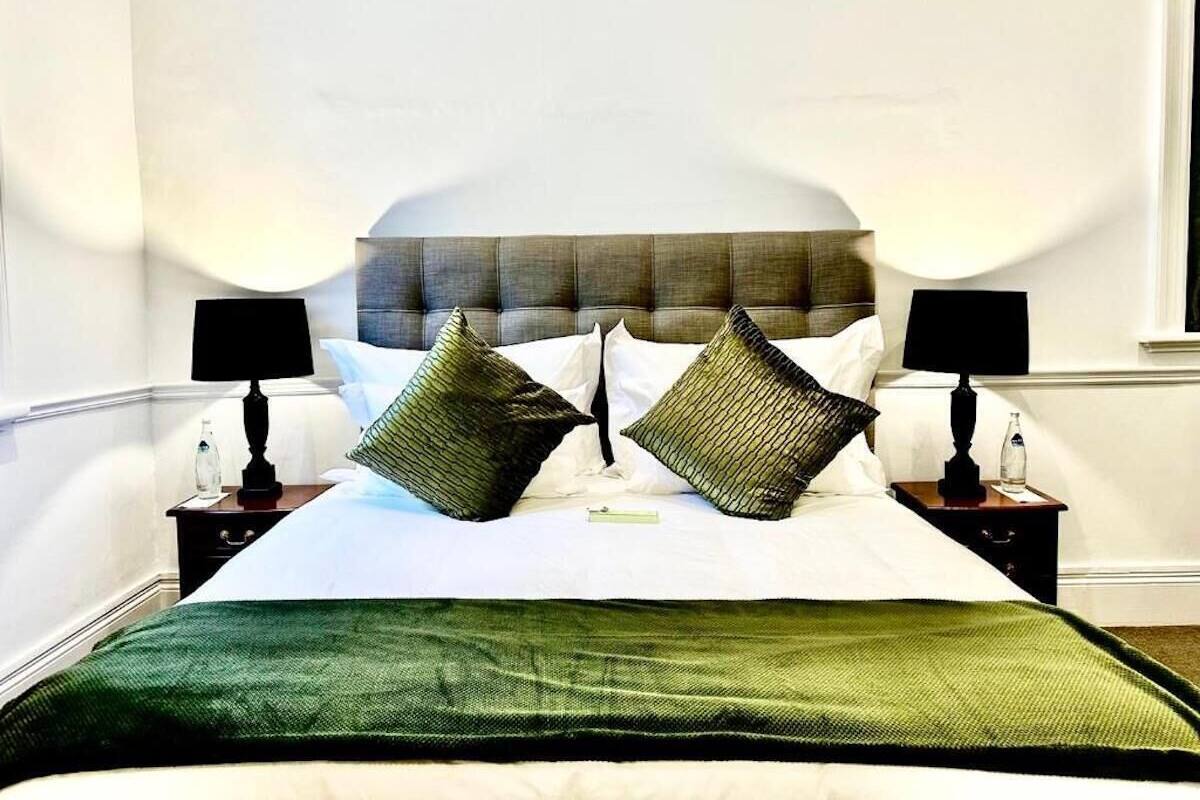 A neatly made bed with a green bedspread, two black lamps on nightstands, and a headboard with a textured design.