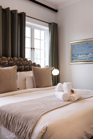 Una habitación de hotel con una cama grande, una ventana con cortinas, un cuadro del mar y una lámpara.
