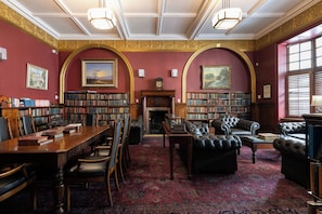 Una biblioteca con estanterías, chimenea, mobiliario de cuero y alfombra estampada.