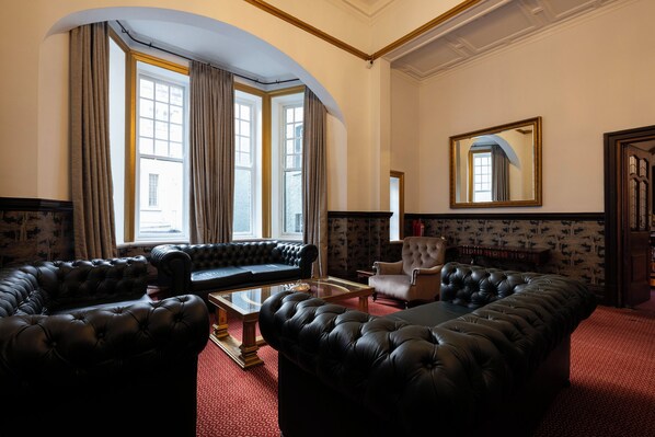 A room with a large black leather sofa, a smaller sofa, a glass coffee table, and a patterned wallpaper. - The Cape Town Club (Cape Town)
