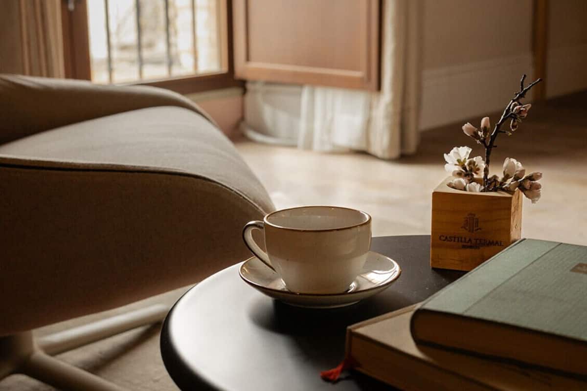 A cozy room with a sofa, a round table with a cup and books, and a window with curtains.