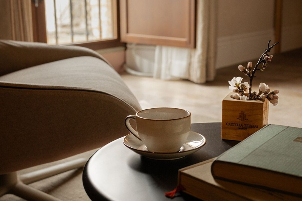 A cozy room with a sofa, a round table with a cup and books, and a window with curtains.