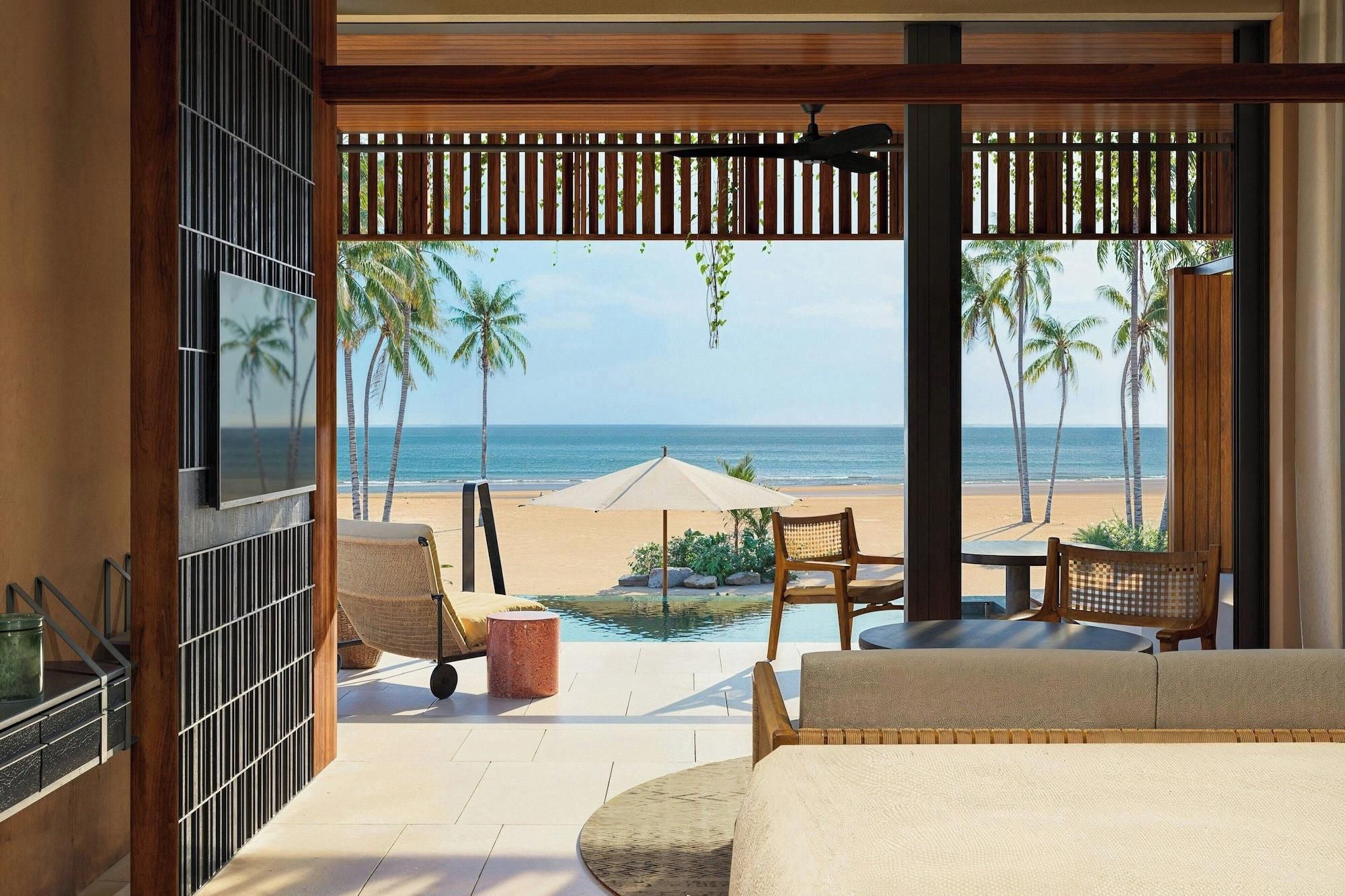 A room with a view of the beach, a pool, and a ceiling fan.