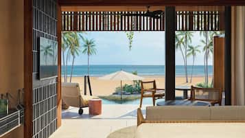 A room with a view of the beach, a pool, and a ceiling fan.
