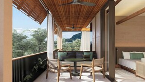 A balcony with a wooden ceiling, a round table, two chairs, a sofa, and a view of trees and mountains.